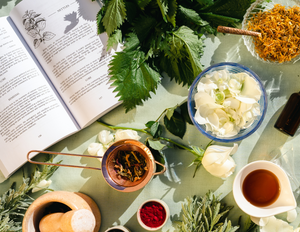an herbal dictionary book is open on a table with bowls and jars of plants and herbal medicine